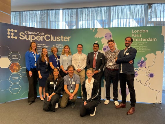 Eleven people who work for Cambridge Cleantech posing in front of a poster for the Climate Tech Super Cluster